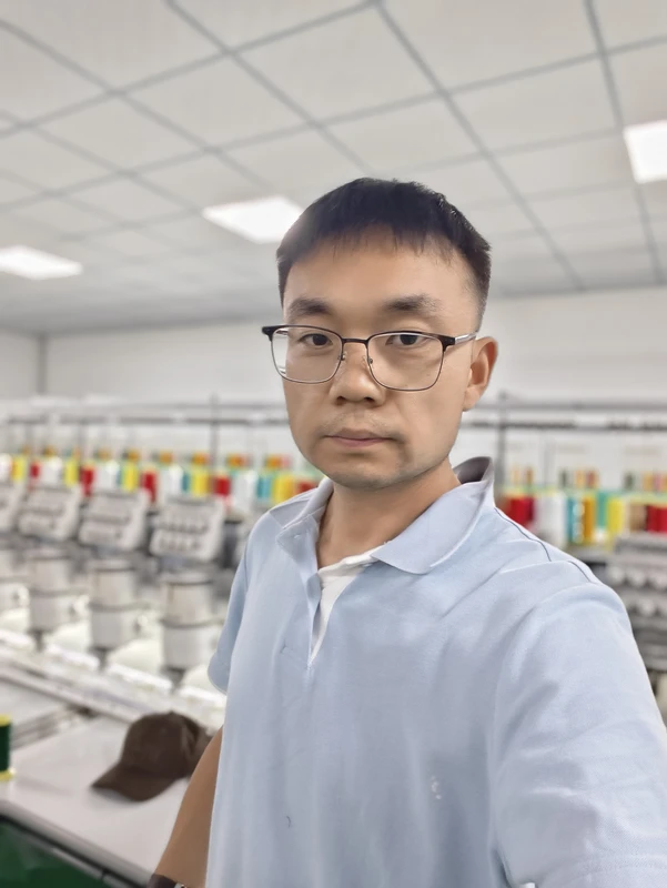 Carson Feng standing in the BDBRIM embroidery workshop with machines behind him