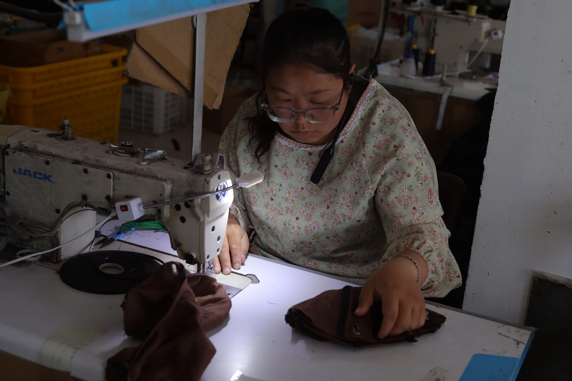 Operator guiding brown cap pieces at an industrial sewing machine in the factory