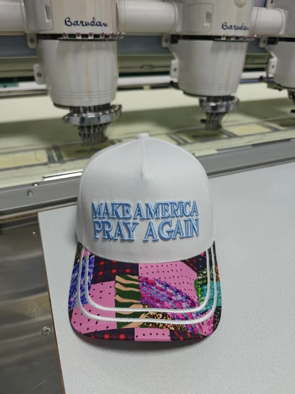 White baseball cap with light blue front embroidery and a colourful printed-pattern visor photographed in an embroidery workshop