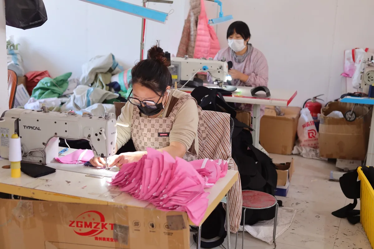 An operator sewing pink cap components beside a stack of matching pieces
