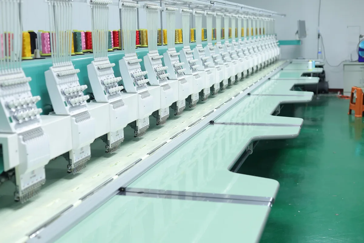 A row of embroidery machine heads with thread cones in the BDBRIM workshop