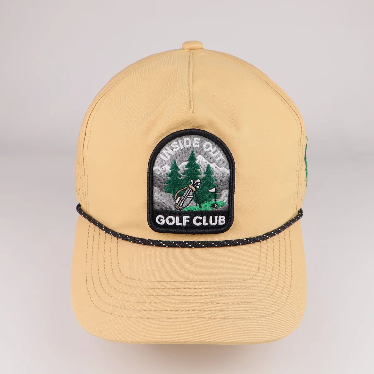 Tan golf cap with circular front crest, dark rope trim and curved visor