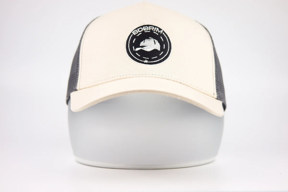 Front view of cream and gray mesh trucker cap with round black embroidery patch