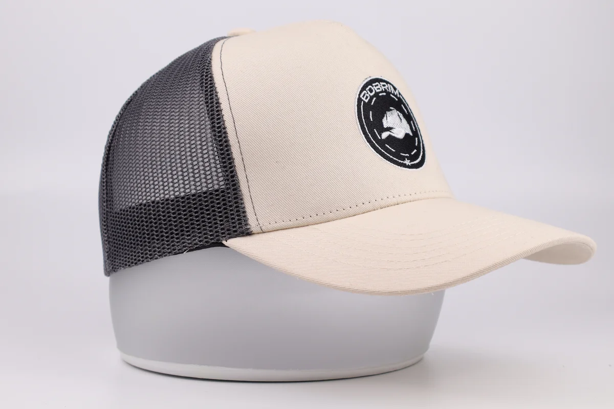 Side profile of cream trucker cap with gray mesh back and round embroidered logo