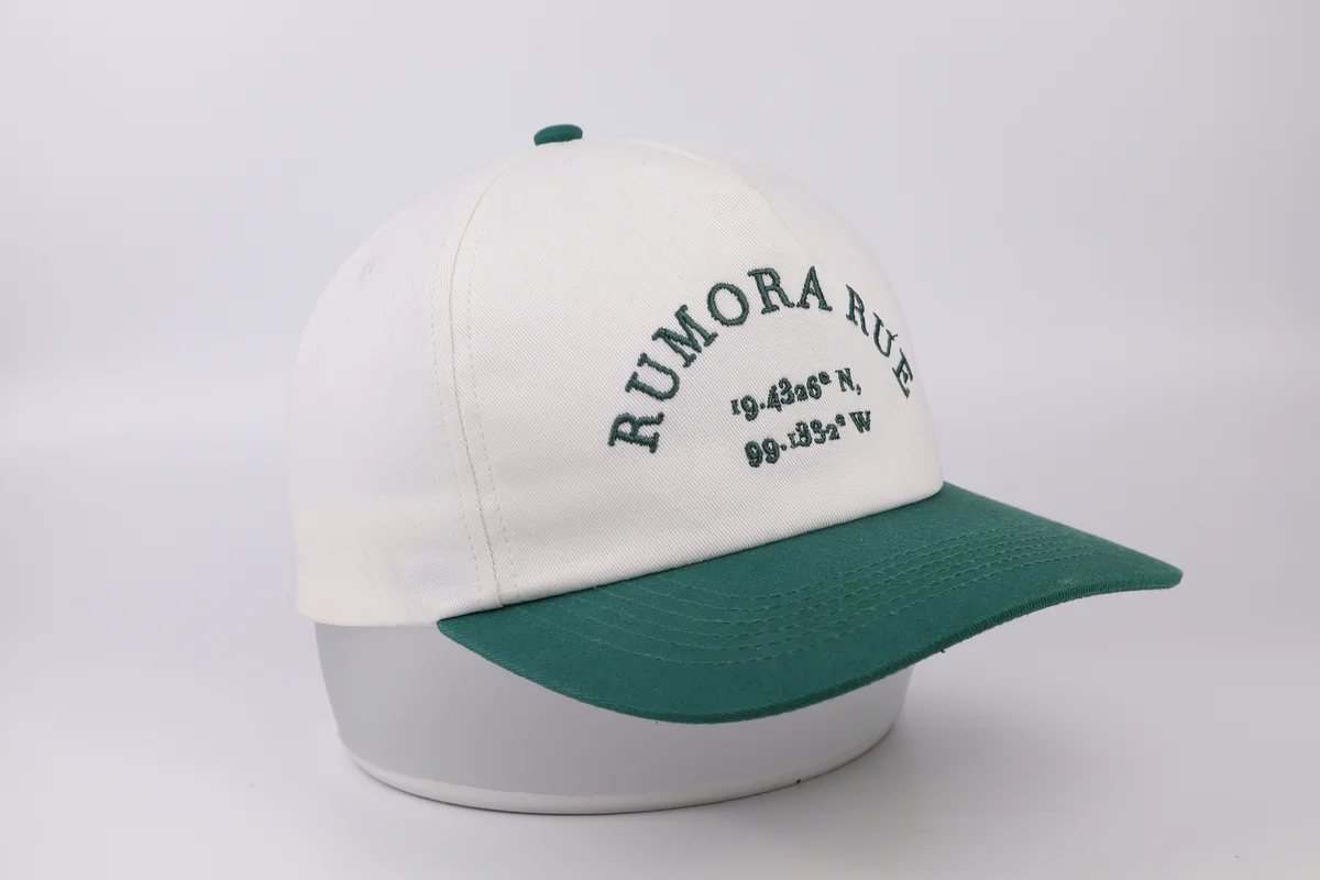Cream baseball cap with green curved visor and arched green front embroidery