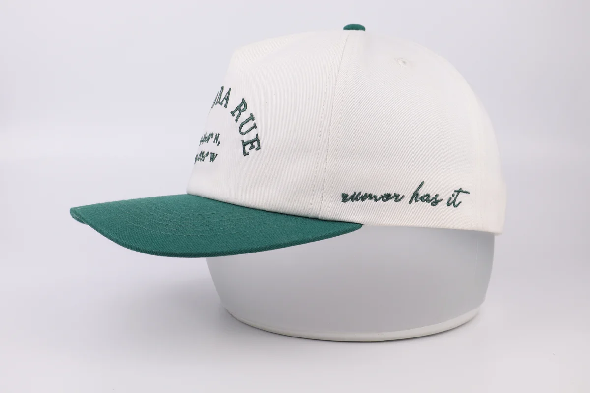 Side profile of a cream baseball cap with dark green visor and side embroidery